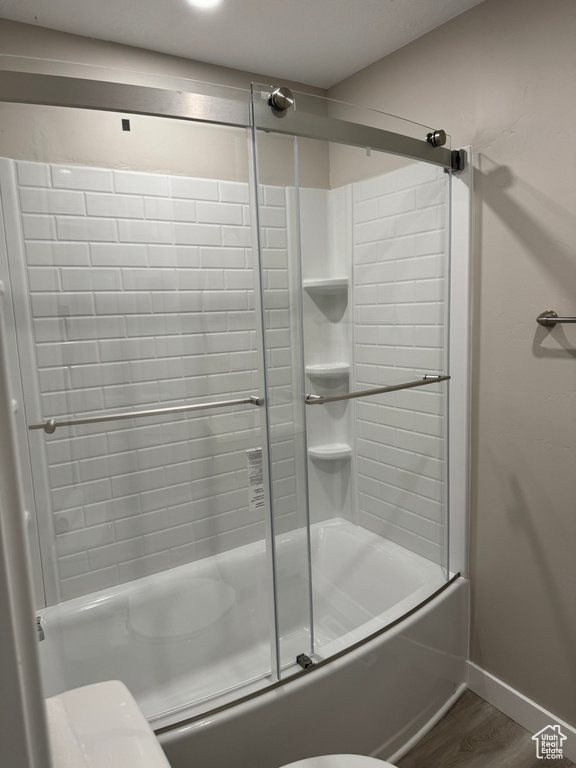 Bathroom featuring toilet, shower / bath combination with glass door, and hardwood / wood-style flooring