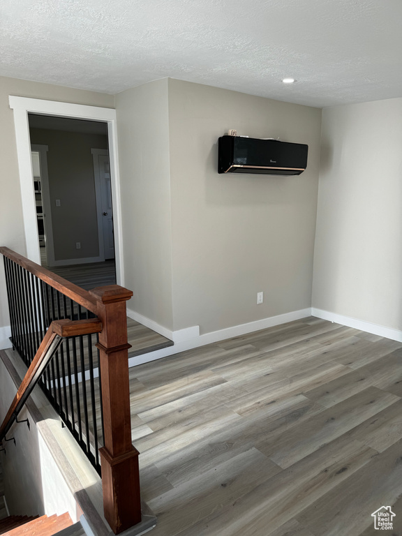 Stairway featuring a textured ceiling, a wall unit AC, and light hardwood / wood-style floors
