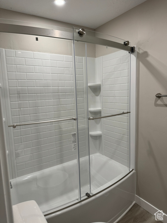 Bathroom featuring shower / bath combination with glass door, hardwood / wood-style flooring, and toilet