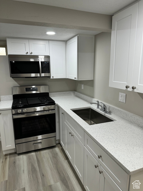 Kitchen with white cabinetry, sink, light wood-type flooring, and appliances with stainless steel finishes