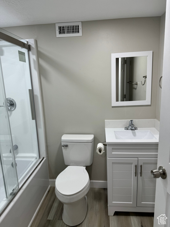 Full bathroom featuring vanity, toilet, bath / shower combo with glass door, and wood-type flooring