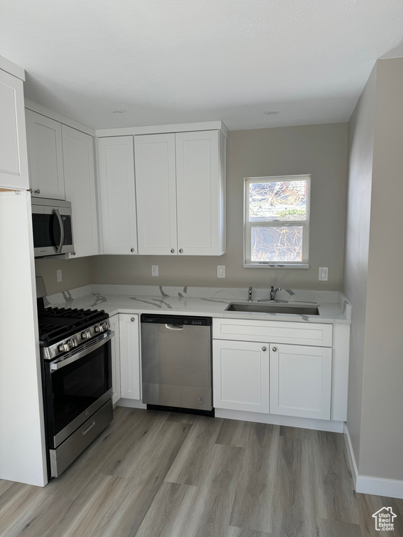 Kitchen featuring sink, white cabinets, stainless steel appliances, and light hardwood / wood-style flooring