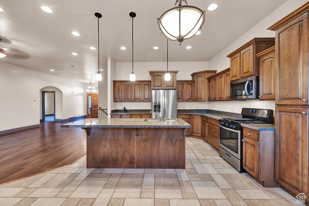 Kitchen with pendant lighting, stainless steel appliances, a kitchen island with sink, and light tile floors
