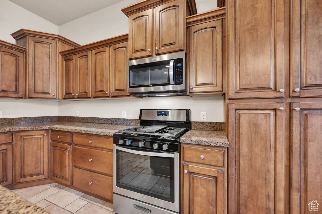 Kitchen featuring dark stone countertops, stainless steel appliances, and light tile flooring