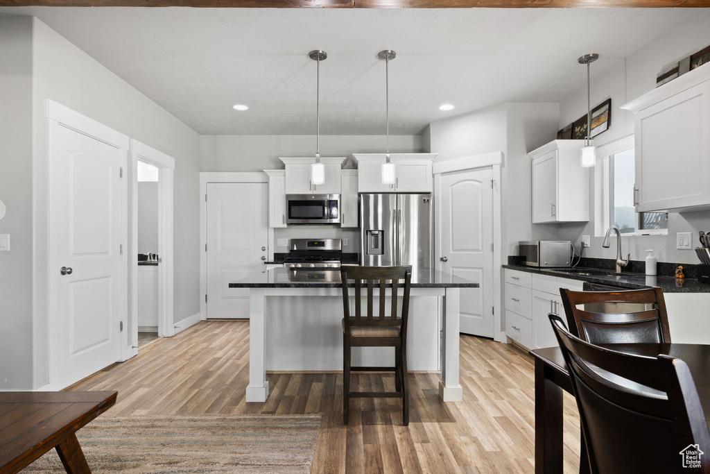 Kitchen featuring white cabinets, pendant lighting, light hardwood / wood-style flooring, appliances with stainless steel finishes, and a kitchen bar