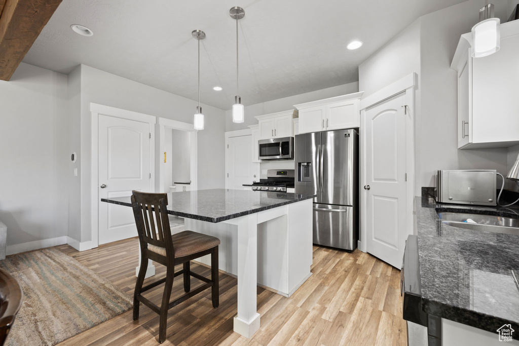 Kitchen with light wood-type flooring, white cabinetry, stainless steel appliances, and pendant lighting