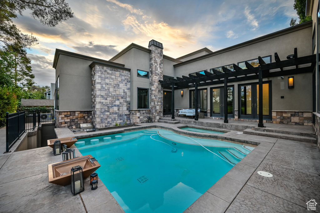 Pool at dusk with a patio area, an in ground hot tub, and a pergola