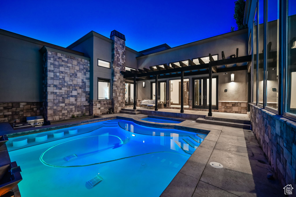 Pool at night with a pergola, an in ground hot tub, and a patio area
