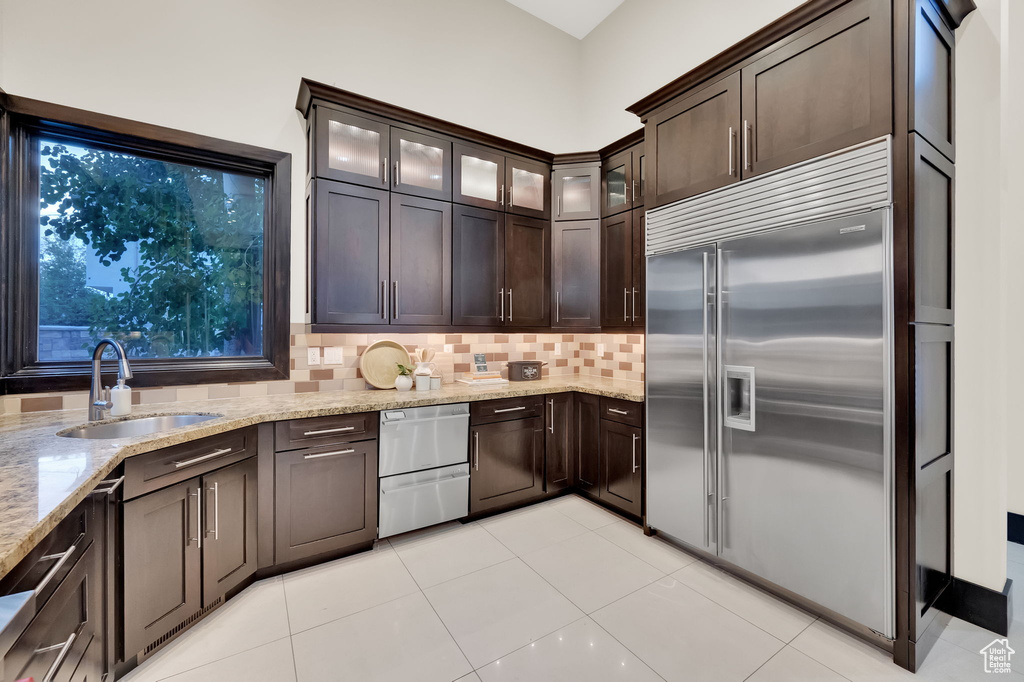 Kitchen featuring stainless steel built in refrigerator, sink, light stone countertops, backsplash, and light tile floors