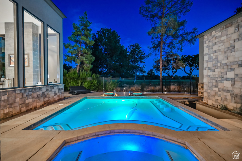 Pool at night featuring a patio and an in ground hot tub