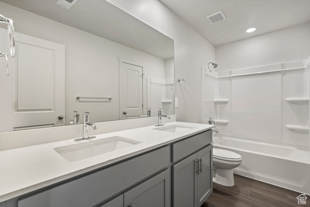 Full bathroom with large vanity, double sink, toilet, shower / bathtub combination, and hardwood / wood-style flooring