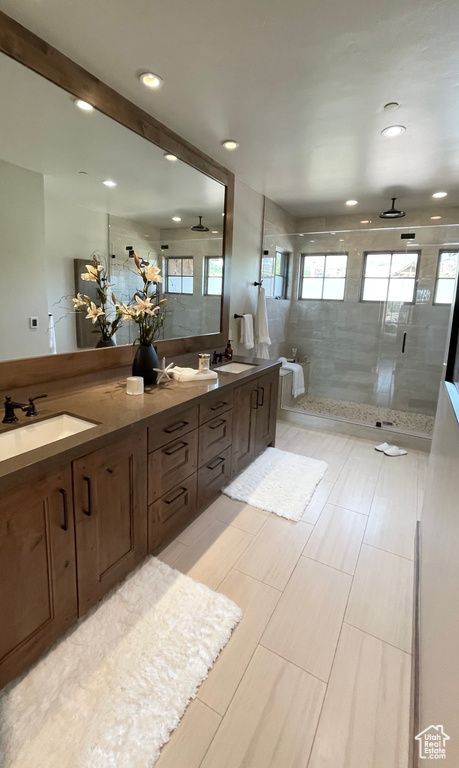 Bathroom featuring a shower with shower door, ceiling fan, vanity, and tile patterned floors