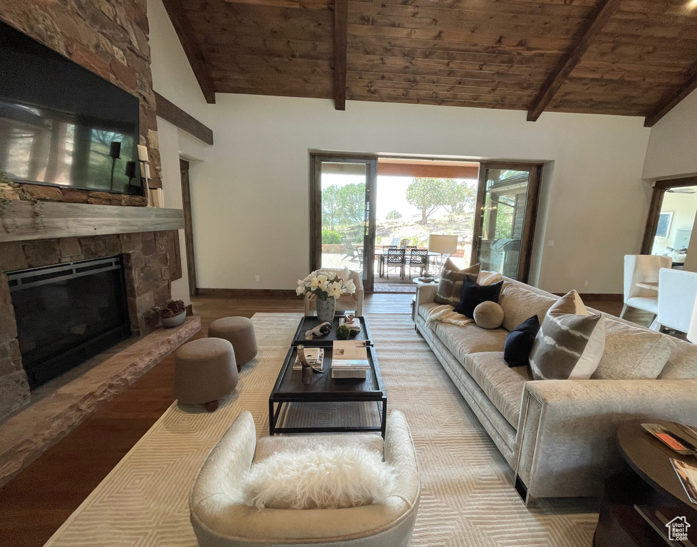 Living room featuring wood ceiling, a stone fireplace, vaulted ceiling with beams, and light hardwood / wood-style floors