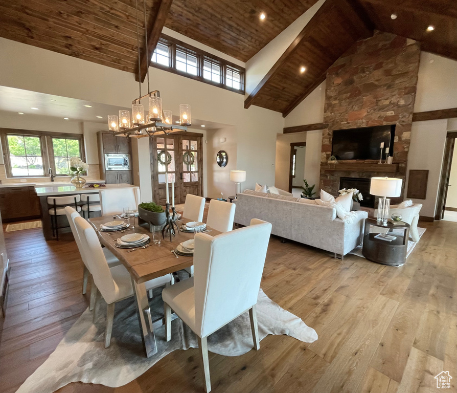 Dining room with a fireplace, light wood-type flooring, high vaulted ceiling, a notable chandelier, and wood ceiling