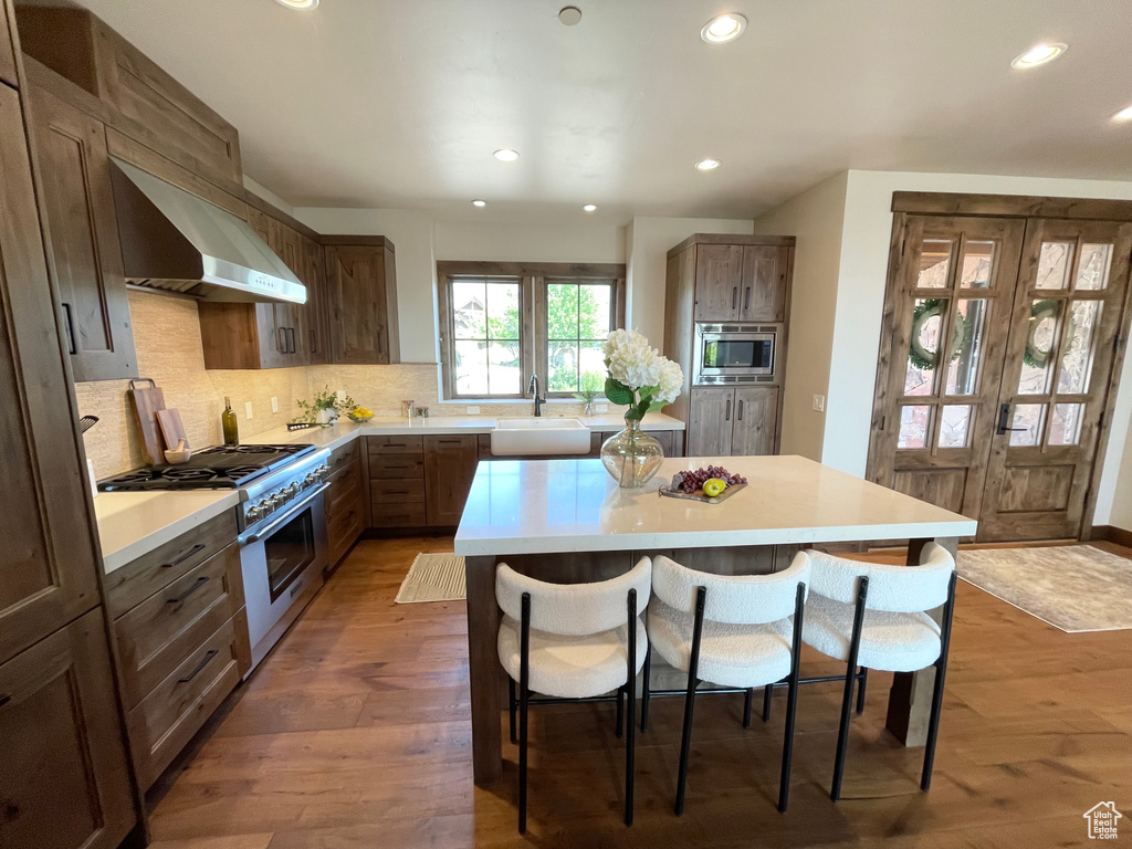 Kitchen featuring a kitchen island, stainless steel appliances, wall chimney range hood, and hardwood / wood-style flooring