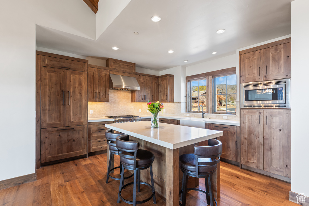 Kitchen with a kitchen breakfast bar, appliances with stainless steel finishes, wall chimney exhaust hood, a kitchen island, and dark hardwood / wood-style flooring