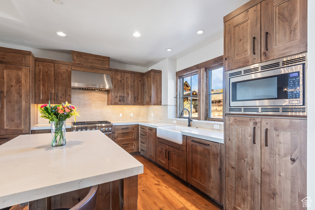 Kitchen with wall chimney range hood, stainless steel appliances, sink, tasteful backsplash, and light hardwood / wood-style flooring