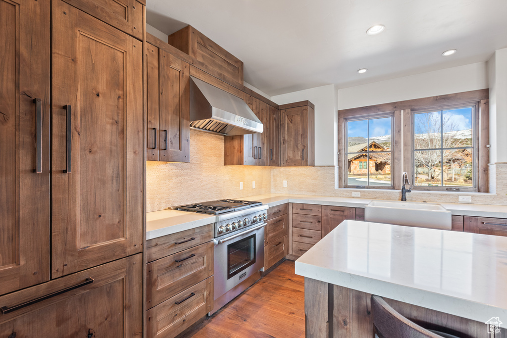 Kitchen featuring light hardwood / wood-style flooring, sink, tasteful backsplash, stainless steel range, and wall chimney range hood