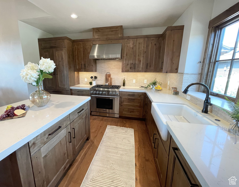 Kitchen featuring high end stainless steel range, backsplash, wood-type flooring, and wall chimney range hood