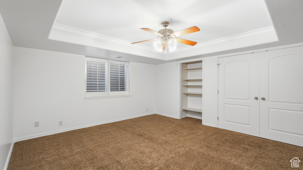 Unfurnished bedroom with a raised ceiling, ceiling fan, crown molding, and dark carpet