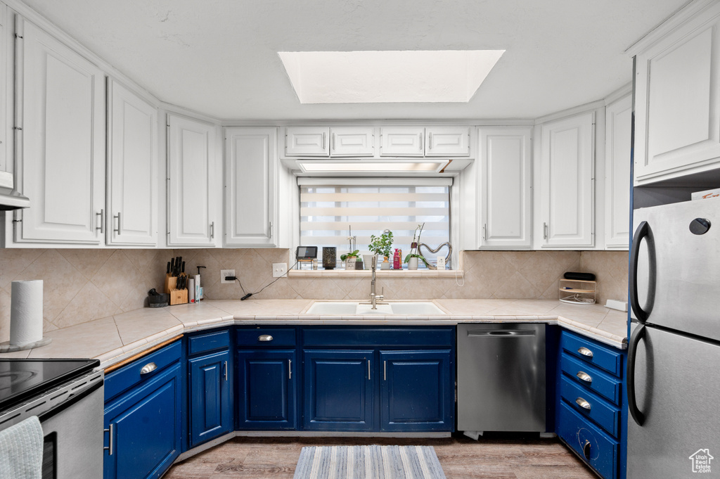 Kitchen with appliances with stainless steel finishes, blue cabinetry, light hardwood / wood-style flooring, sink, and a skylight