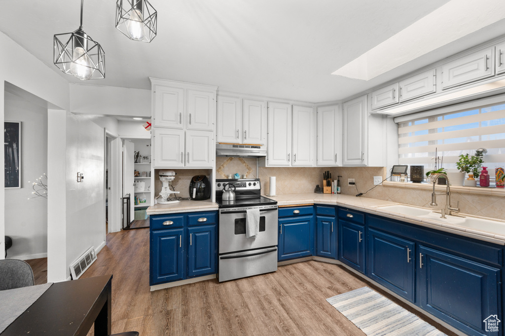 Kitchen with electric range, white cabinets, blue cabinets, decorative light fixtures, and light hardwood / wood-style floors