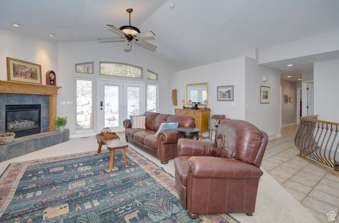 Living room with ceiling fan, french doors, high vaulted ceiling, a tiled fireplace, and light tile floors