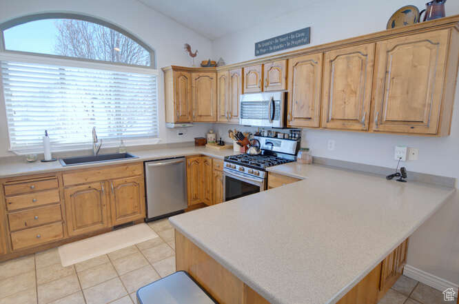 Kitchen with sink, light tile flooring, appliances with stainless steel finishes, and kitchen peninsula