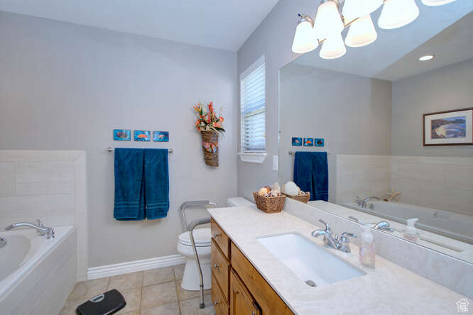 Bathroom featuring tile flooring, vanity with extensive cabinet space, toilet, a notable chandelier, and tiled bath
