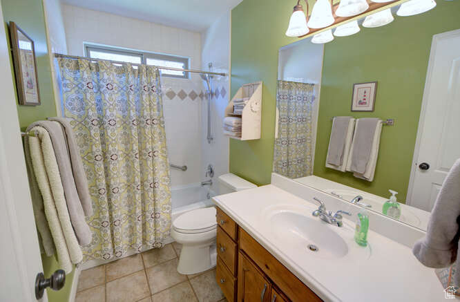 Full bathroom with tile flooring, vanity with extensive cabinet space, shower / tub combo with curtain, and toilet