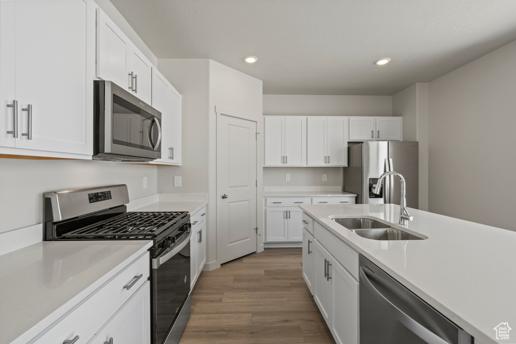 Kitchen with sink, appliances with stainless steel finishes, hardwood / wood-style flooring, and white cabinetry