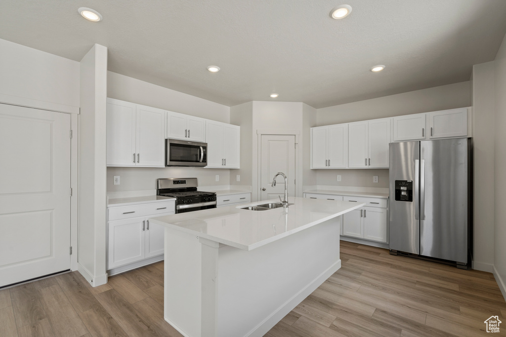 Kitchen featuring a center island with sink, appliances with stainless steel finishes, light wood-type flooring, and white cabinetry
