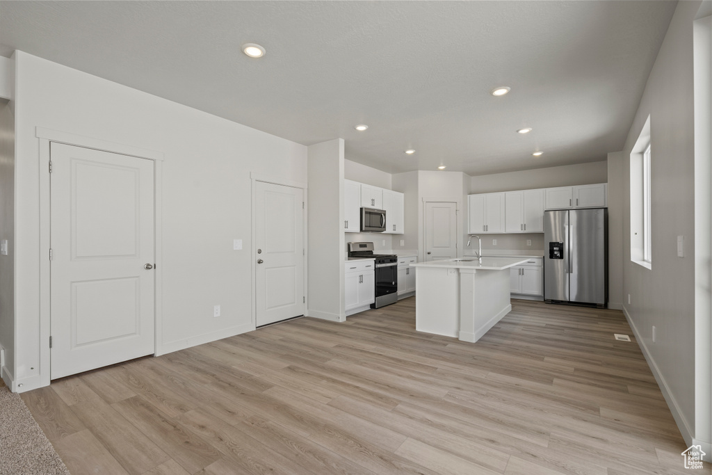 Kitchen with white cabinets, an island with sink, light hardwood / wood-style flooring, and stainless steel appliances