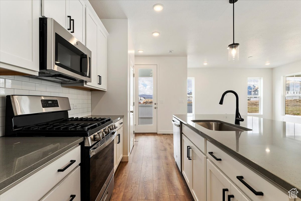 Kitchen with appliances with stainless steel finishes, backsplash, white cabinetry, dark hardwood / wood-style floors, and pendant lighting