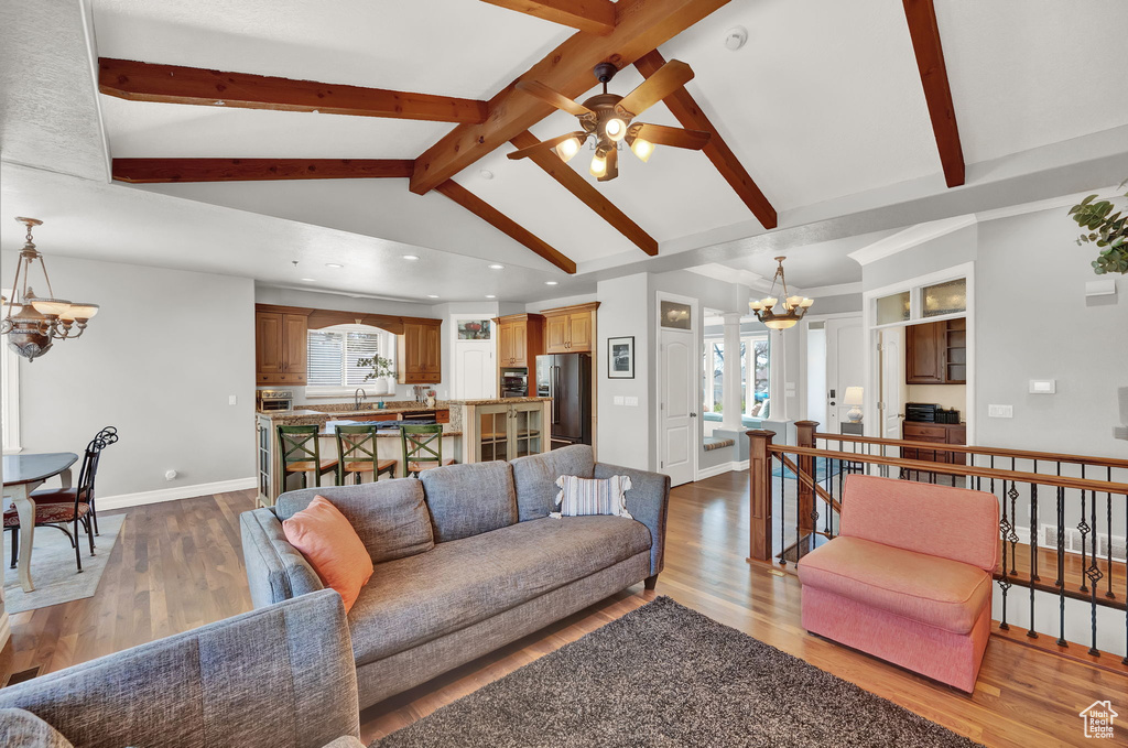Living room with ceiling fan with notable chandelier, hardwood / wood-style floors, and vaulted ceiling with beams