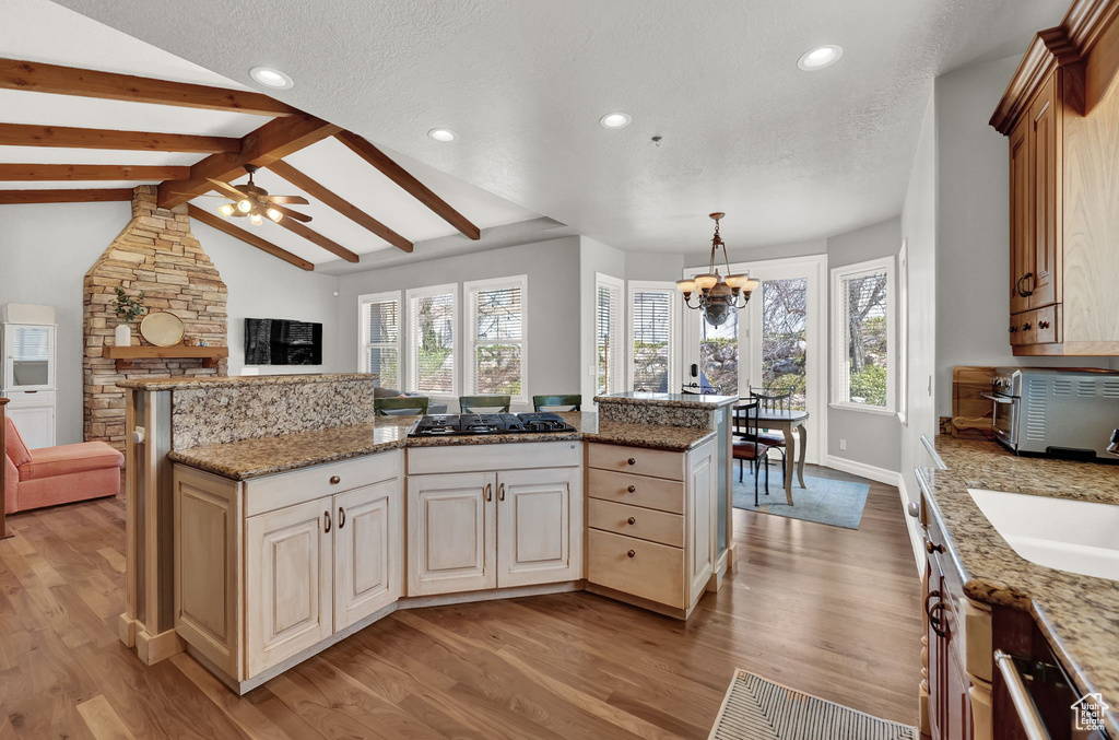 Kitchen with light hardwood / wood-style floors, beam ceiling, light stone counters, and a healthy amount of sunlight
