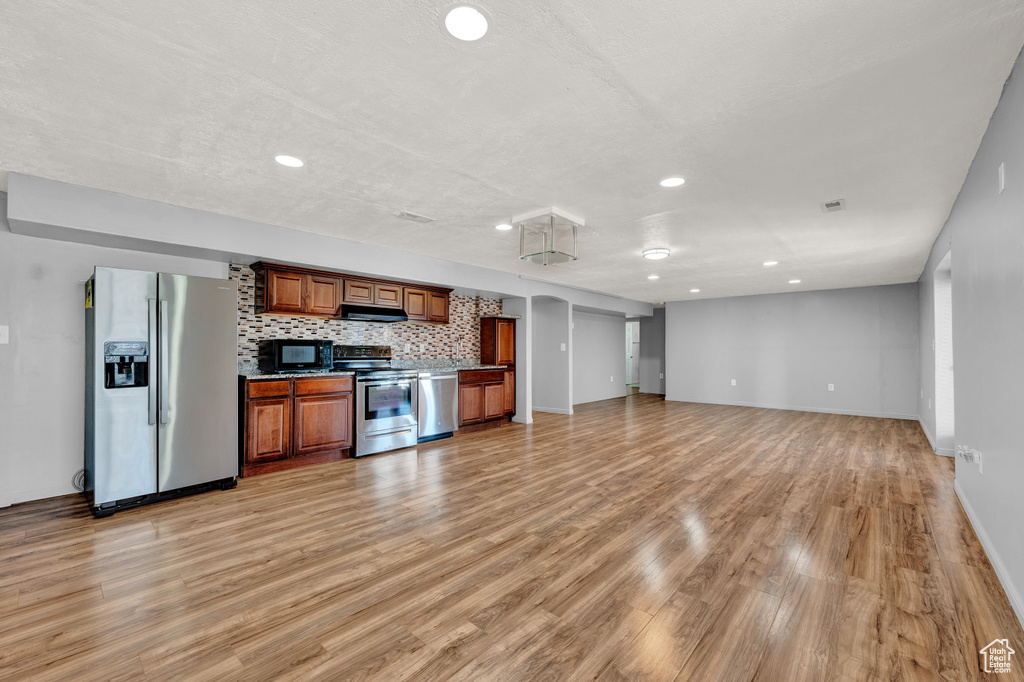 Kitchen with backsplash, appliances with stainless steel finishes, and light hardwood / wood-style flooring