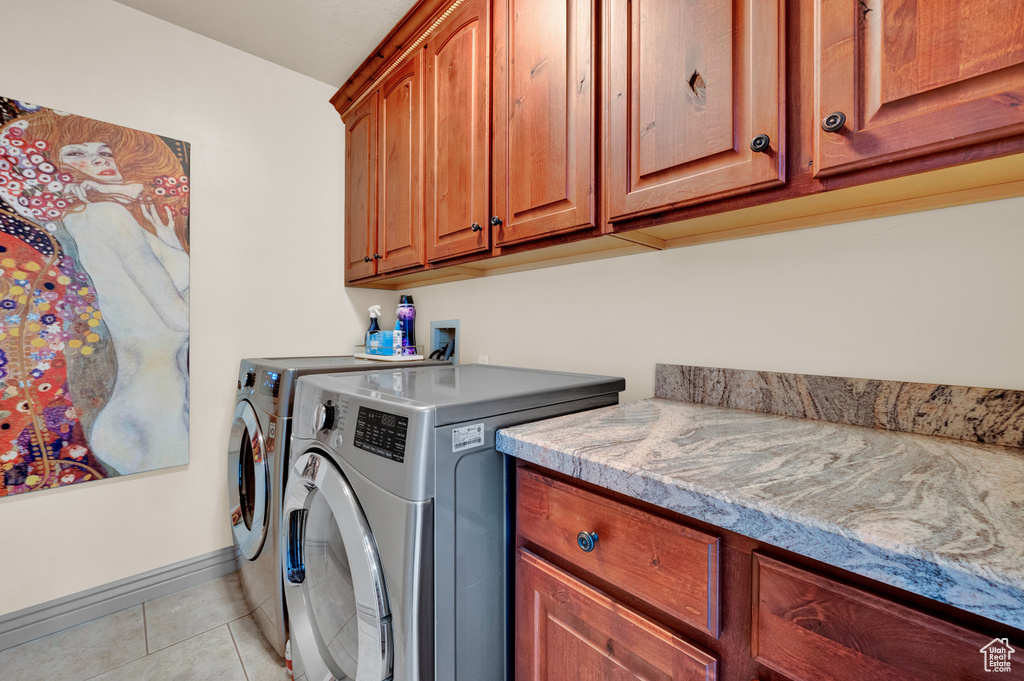 Clothes washing area with cabinets, washing machine and dryer, light tile floors, and hookup for a washing machine