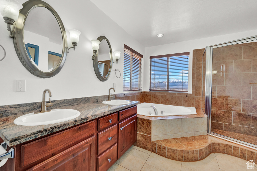 Bathroom with tile flooring, double sink, vanity with extensive cabinet space, and separate shower and tub