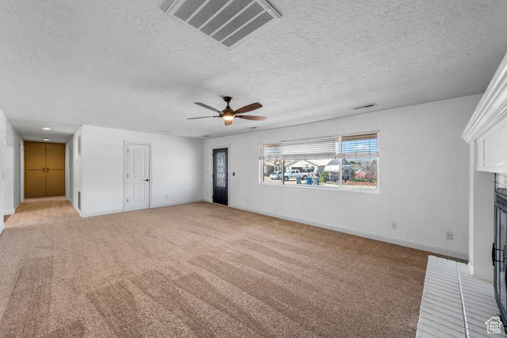 Unfurnished living room featuring a textured ceiling, light colored carpet, and ceiling fan