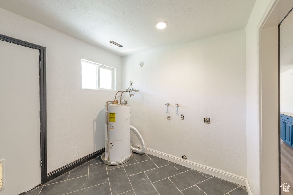Laundry area featuring water heater, dark tile floors, and washer hookup