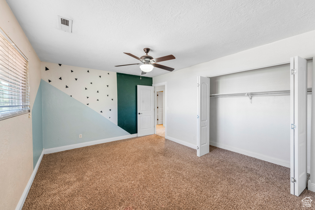 Unfurnished bedroom with a closet, light carpet, a textured ceiling, and ceiling fan