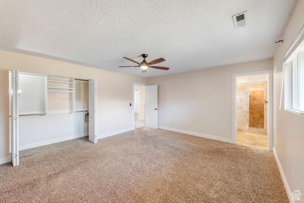 Unfurnished bedroom with ensuite bath, light colored carpet, a textured ceiling, and ceiling fan