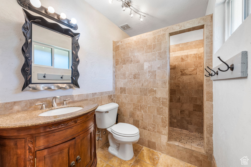 Bathroom with tile walls, vanity, tiled shower, tile floors, and toilet