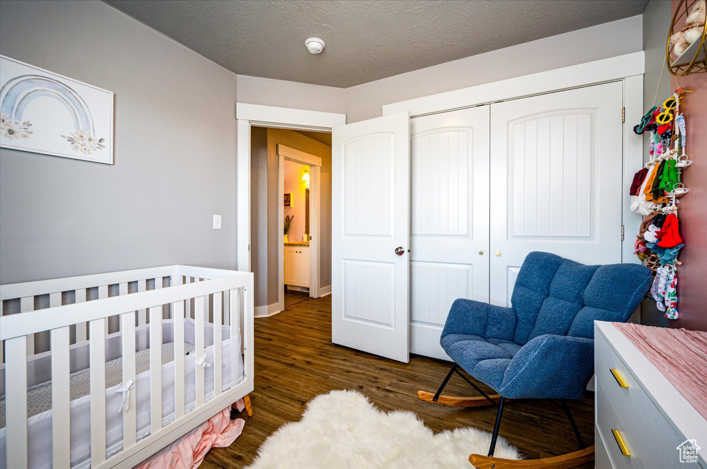 Bedroom featuring a textured ceiling, a nursery area, a closet, and dark hardwood / wood-style flooring