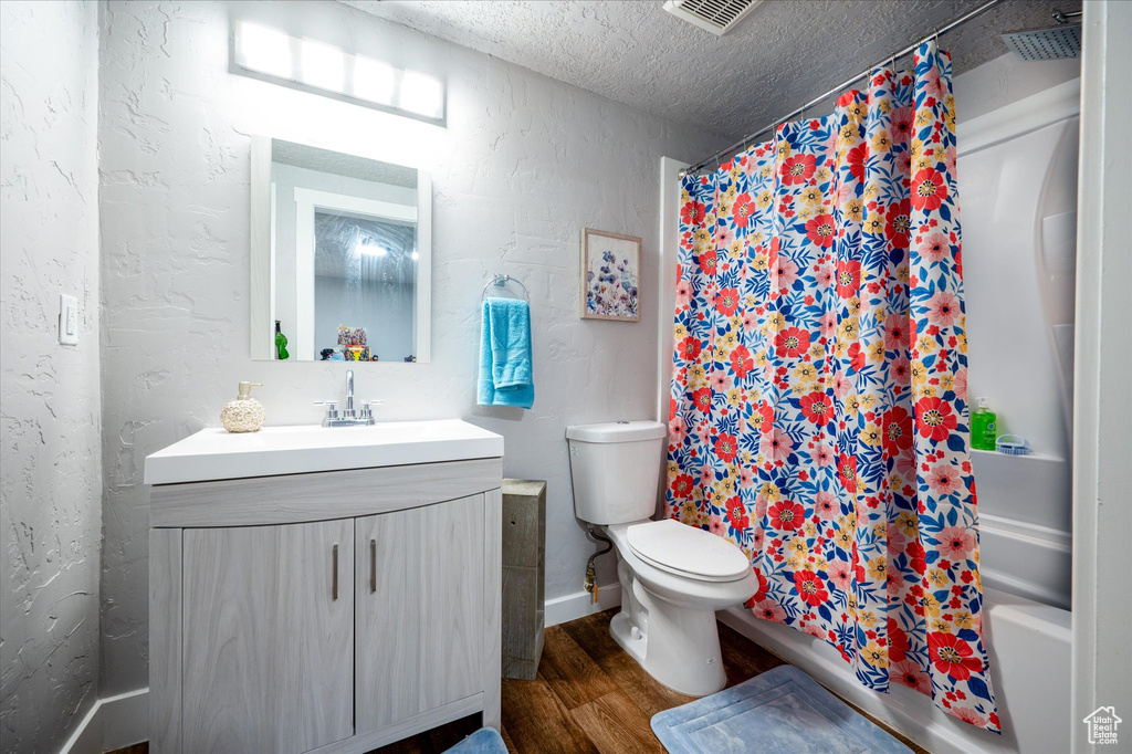 Full bathroom with hardwood / wood-style floors, vanity, a textured ceiling, shower / bathtub combination with curtain, and toilet