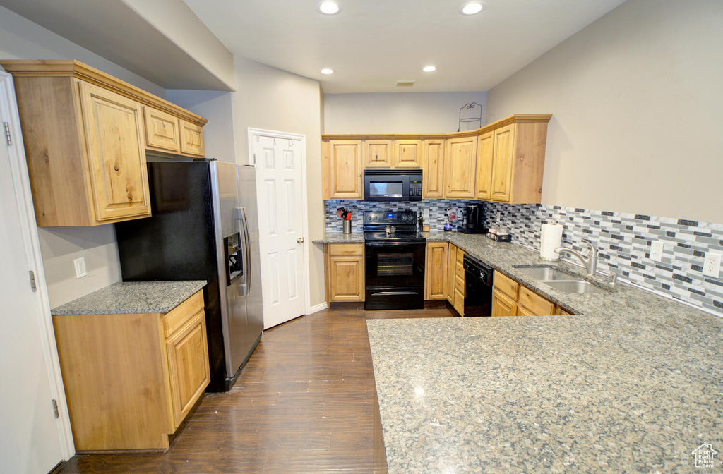 Kitchen featuring dark hardwood / wood-style floors, light stone counters, sink, black appliances, and tasteful backsplash