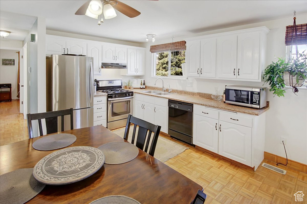 Kitchen featuring white cabinets, ceiling fan, stainless steel appliances, light parquet flooring, and sink