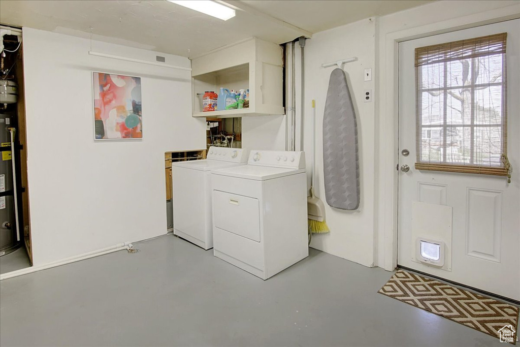 Clothes washing area featuring washer and dryer, water heater, and cabinets
