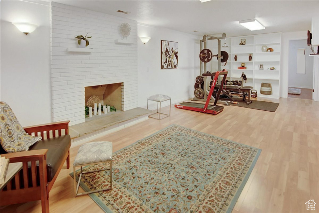 Interior space with a brick fireplace, brick wall, built in shelves, and light hardwood / wood-style floors
